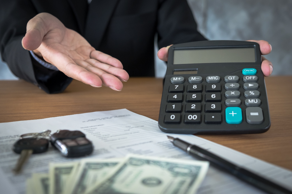 Hand gesturing beside a calculator, car keys, and a loan document, representing refinancing a car loan