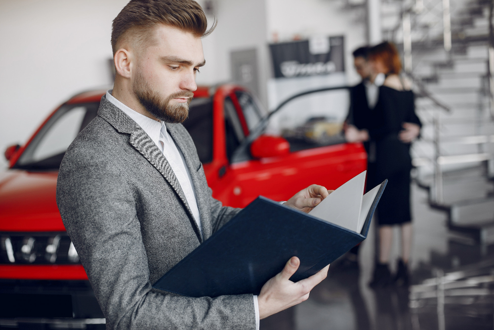 Finance manager reviewing auto loan paperwork beside a car in a dealership showroom, representing how auto loan interest rates get finalized