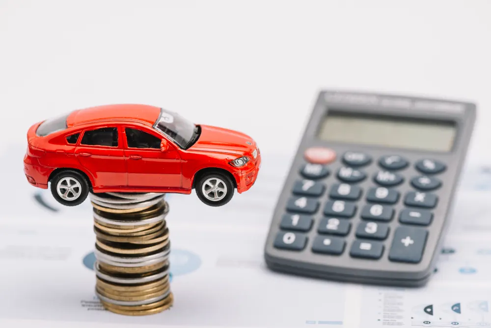 Toy car balanced on a stack of coins next to a calculator, symbolizing car insurance cost