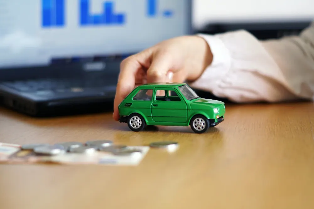 Hand holding a toy car in front of a laptop, representing car insurance and buying guides