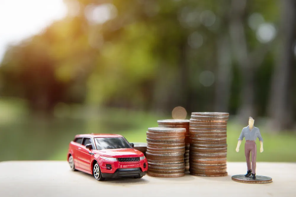 Miniature figure beside a toy SUV and stacks of coins outdoors, representing car ownership costs