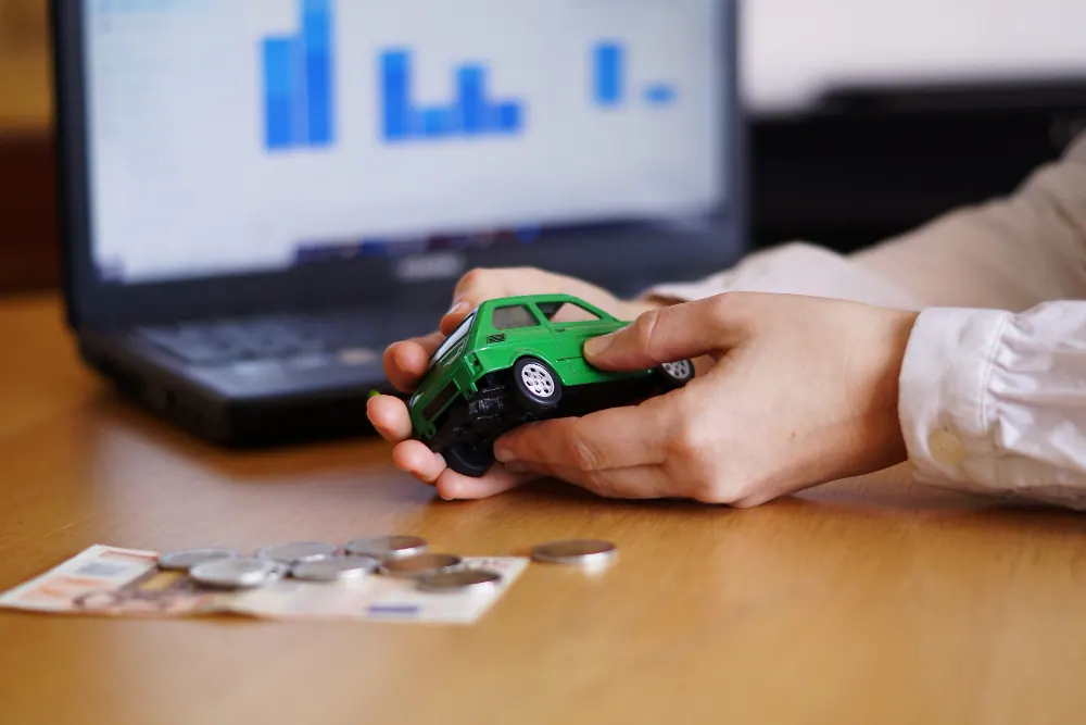 Two hands holding a toy car in front of a laptop showing financial charts, representing credit-based insurance scores