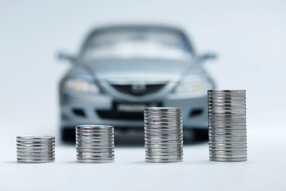 Ascending stacks of coins in front of a car, representing the cost impact of a speeding ticket on insurance