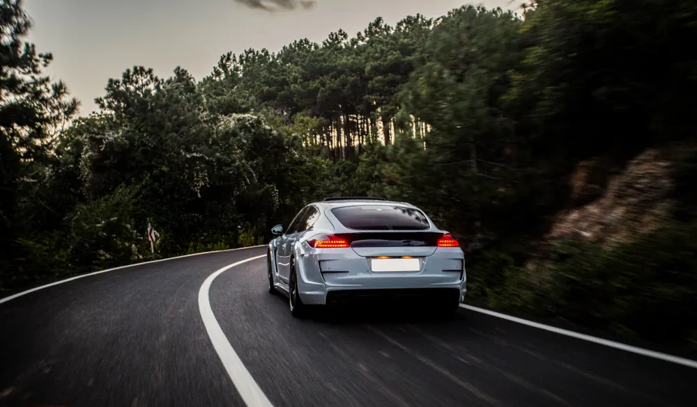Silver sports car driving down a forest road at dusk